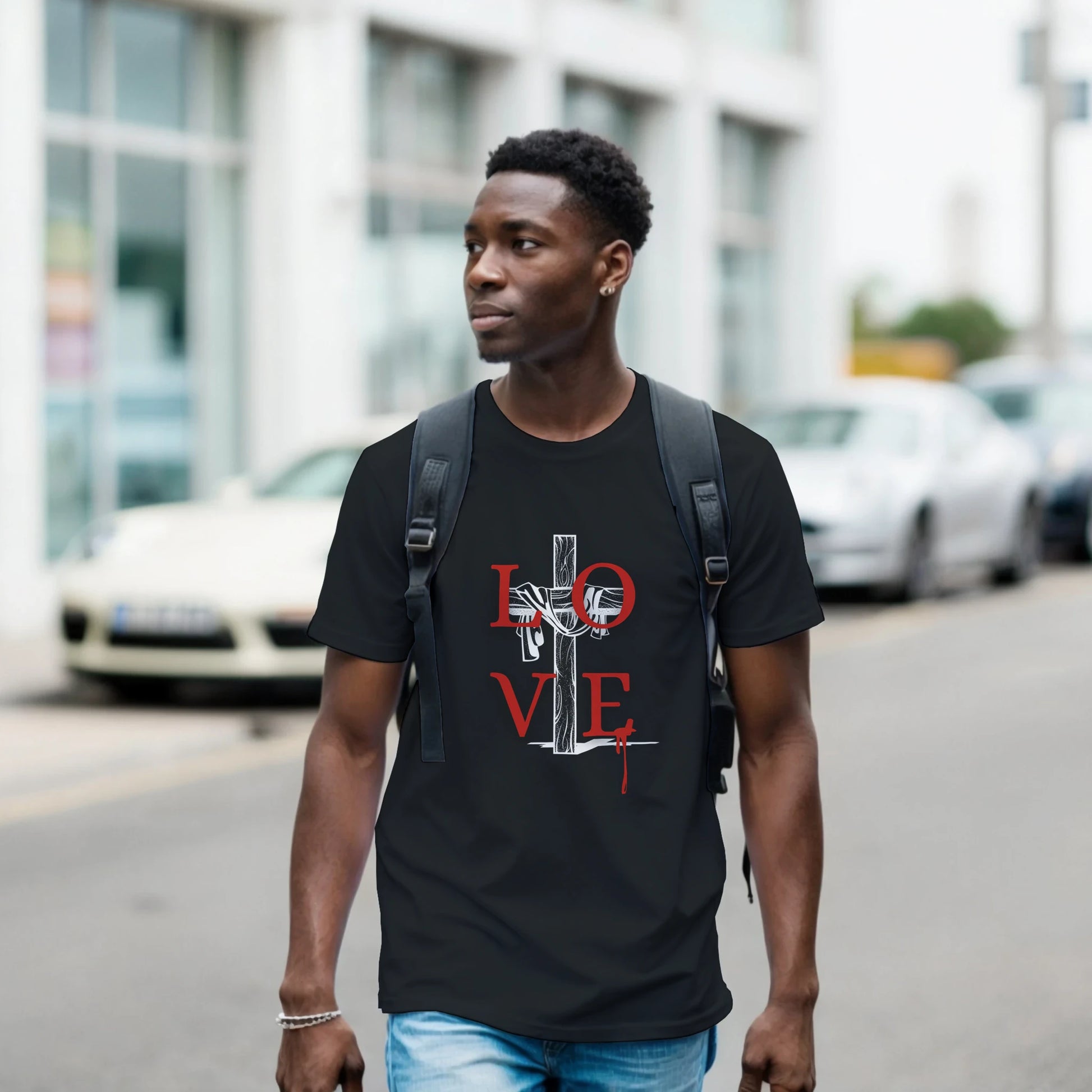 Man wearing a black t-shirt with a graphic Love Crucifixion design walking on a street.