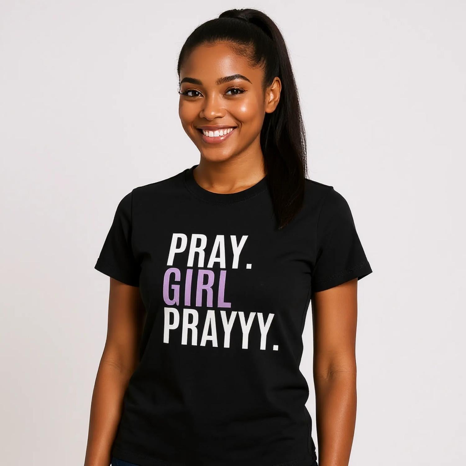 Woman wearing a black t-shirt with 'PRAY. GIRL PRAYYY.' text on a plain background